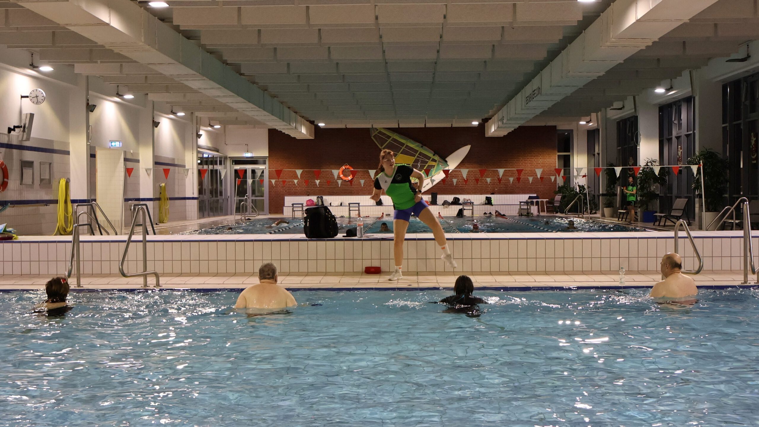 Aquafitnesstraining. 6 Personen im Wasser, eine Trainerin macht Übungen am Beckenrand vor