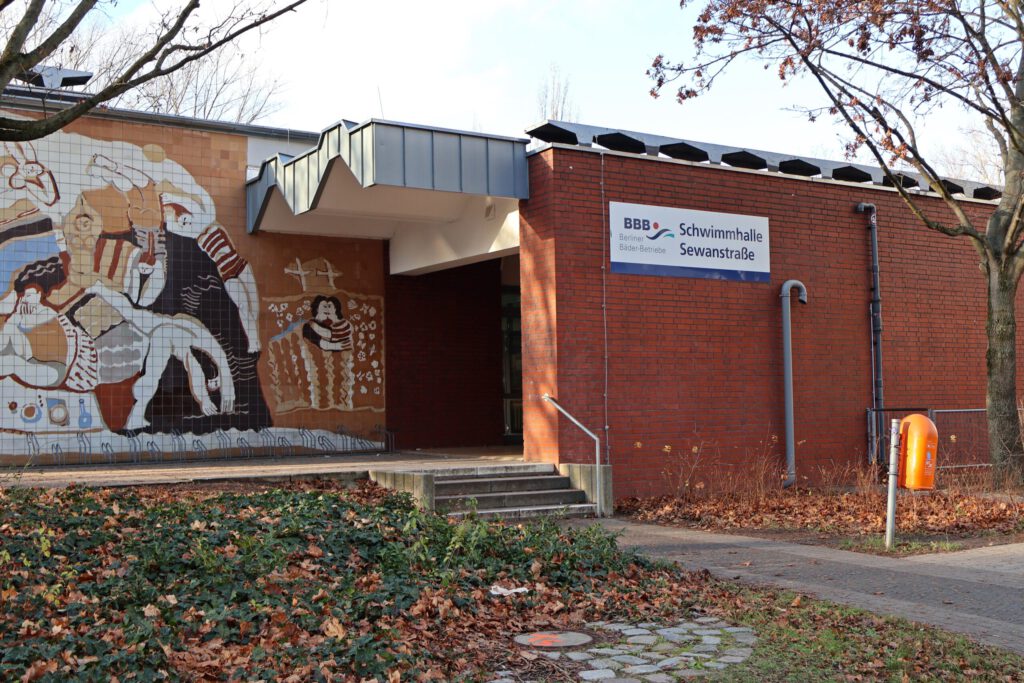 Eingang der Schwimmhalle Sewanstraße, braunes Gebäude, Aufschrift mit Namen und künstlerische Zeichnung an der Hauswand.