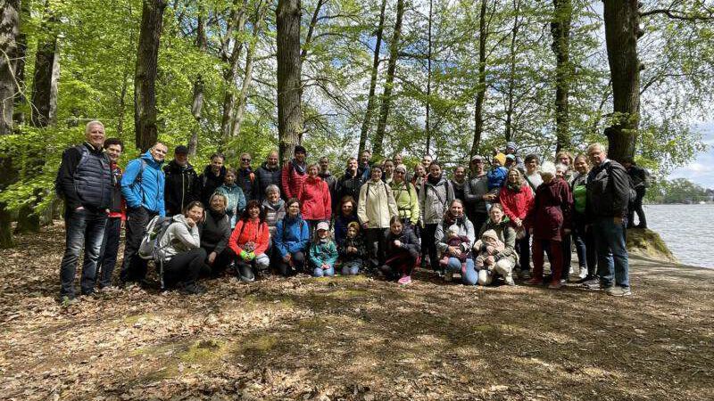 Gruppenbild vom Wandertag 2023. Ca. 40 Menschen verschiedenen Alters stehen auf einer Lichtung im Wald am Ufer.